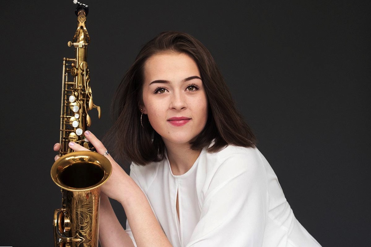 Young woman with a saxophone against dark background