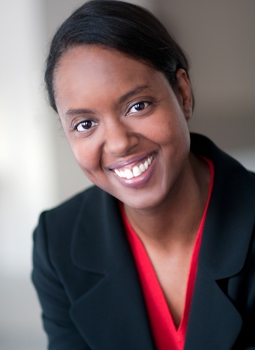 Shows a professional business headshot of a woman wearing a dark suit jacket and a bright red top